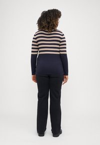 Haut à manches longues à rayures navy avec des rayures horizontales beiges sur la moitié supérieure, associé à un pantalon noir et des chaussures noires. Design texturé et décontracté.