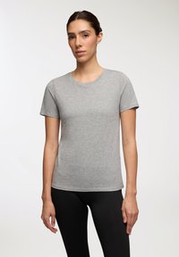 Szara koszulka z krótkim rękawem i okrągłym dekoltem, wykonana z miękkiego materiału. Dopasowany krój w połączeniu z czarnymi legginsami. Minimalistyczny design.