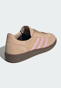 Beige suède sneakers met een ronde neus; heeft drie roze strepen en gele "Spezial" tekst. Rubberen zool met een gestructureerd bruine patroon.
