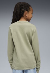Camisa de manga larga en algodón verde claro, con cuello redondo y corte relajado. La parte trasera es lisa, con un diseño simple y limpio.