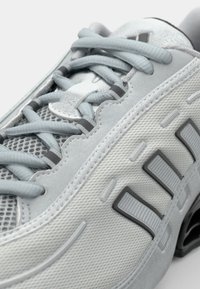 Light gray athletic shoe featuring a textured upper with mesh panels, contrasting dark gray accents, and flat light blue laces.