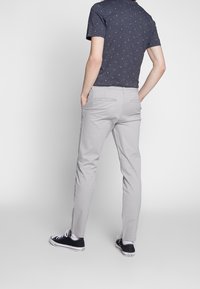 Chinos gris ajustés, avec deux poches à l'arrière. Portés avec un t-shirt sombre à motifs et des baskets noires.