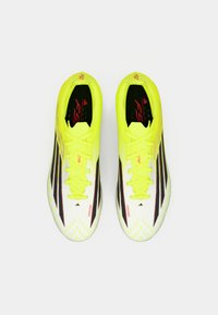 Κίτρινα ποδοσφαιρικά παπούτσια με μαύρες ρίγες, ελαφρύ σχεδιασμό, υφή στην επάνω πλευρά, με κλείσιμο κορδονιών και επώνυμες λεπτομέρειες στην γλώσσα.