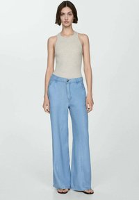 Ljusblå vida jeans i denim med knappstängning, framfickor och en avslappnad passform. Kombinerat med en beige ärmlös topp.