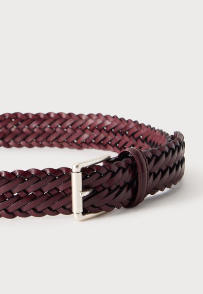 Ceinture en cuir tressé marron foncé avec une boucle en métal argenté et une boucle en cuir assortie sur un fond uni clair.