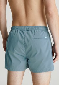 Pantaloni da bagno da uomo in un colore verde teal attenuato, caratterizzati da una vita elastica, tasca sul retro e tessuto liscio e leggero.