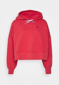 Červená zkrácená mikina z měkké tkaniny, se stahovací kapucí, raglánovými rukávy a malým modrým logem na hrudi.