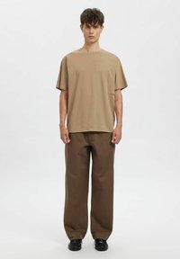 Beežist puuvillast T-särk, mis on lõdva lõikega, laiade lühikeste varrukatega ja väikese logoga. Ühildub lahtiste pruunide pükstega ja mustade kingadega.