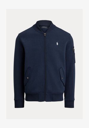 Marineblå sweatshirtjakke med glidelås foran, ribbestrikkede mansjetter og kant, to sidelommer og en glidelåslomme på armen. Har en logo på brystet.