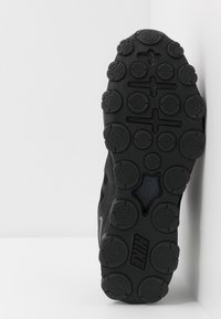 Black athletic shoe sole features textured rubber with circular and hexagonal patterns. Includes a visible Nike logo and rounded lugs for grip.