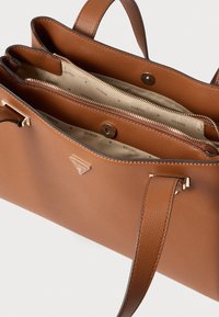 Brązowa torebka ze ziarnistej skóry z dwoma uchwytami, górnym zatrzaskiem i wewnętrzną kieszenią na suwak, z kremową podszewką z nadrukiem logo.