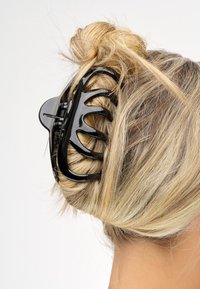 Fibbia per capelli in plastica nera che tiene in posizione uno chignon biondo. La clip presenta un design aperto con denti curvi, offrendo presa e tenuta.