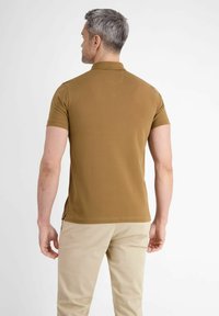 Bruine poloshirt met een korte kraag, getailleerd ontwerp en zijsplitten, gecombineerd met kaki broek. Vlotte textuur, casual stijl.