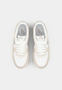 Nike Air Force 1 sneakers med en overdel i hvid læder og beige ruskindede detaljer, flade hvide snørebånd og perforeret tåboks for åndbarhed.
