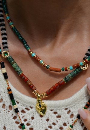 Mehrlagige Halskette mit Perlen in grünen, roten und goldenen Farbtönen sowie einem goldenen Anhänger mit blauen Akzenten. Strukturvolles und farbenfrohes Design.