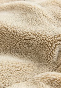 Material din fleece de culoare bej, cu o suprafață moale și texturată, caracterizată prin fire scurte și pufoase și un model ușor reliefat. Ideal pentru căldură și confort.