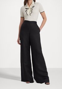 Polo de couleur claire avec col à volants et bordure noire, associé à un pantalon noir à jambes larges. Tissu lisse avec une coupe décontractée.