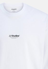 Bijela pamučna majica s okruglim izrezom, s malim crnim logotipom "JJ Studios" na prednjoj strani, meke teksture i opuštenog kroja.