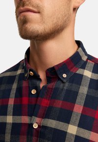 Karierte Hemd in marineblau, rot und beige; aus strukturiertem Stoff mit Button-Down-Kragen und Holzknöpfen.