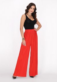 Red pleated wide-leg pants paired with a black fitted tank top. Accessories include a chunky necklace and a bracelet. Black heeled shoes.