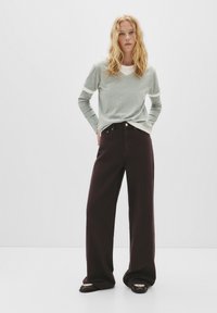 Siva dolgi rokav s belimi detajli, v kombinaciji z širokimi borovničnimi hlačami. Oblačilo ima sproščen kroj in gladke teksture.