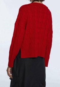 Pull en maille rouge avec motif en torsades, ourlet côtelé et manches longues. Présente un dos court et une surface texturée.