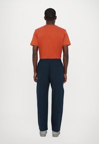Männeroutfit bestehend aus einem orangefarbenen kurzärmeligen T-Shirt und einer navyblauen Jogginghose. Die Hose hat einen elastischen Bund; beide Teile sind Freizeitkleidung.