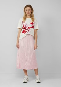 T-shirt blanc avec un imprimé floral rouge, associé à une jupe midi plissée rose. Le mannequin porte des baskets de couleur claire.