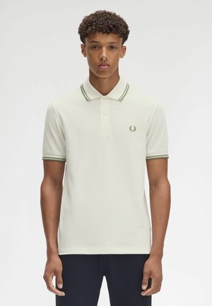 Polo in cotone bianco sporco con colletto e polsini a righe verdi, caratterizzato da un discreto logo ricamato sul lato sinistro del petto.