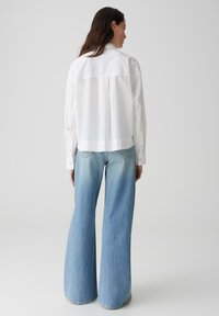 Witte kraagloze blouse met lange mouwen, knoopdetails en lichtblauwe flared jeans, met een vervaagde was en wijde pijpen.