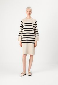 Beige stripete strikkekjole med svarte horisontale striper, vide ermer og avslappet passform. Skoene har myke beige sko med stroppe-detalj.