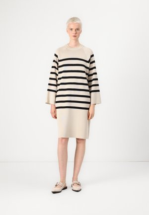 Beige stripete strikkekjole med svarte horisontale striper, vide ermer og avslappet passform. Skoene har myke beige sko med stroppe-detalj.