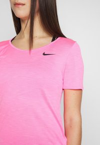 Rosa idrottströja med korta ärmar, tillverkad av texturerat material. Har en svart Nike-logotyp på övre vänstra sidan.