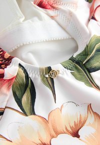 Țesătură cu model floral în nuanțe de piersică, roz și verde. Previne o închidere metalică cu un design circular. Textură moale, ușoară.