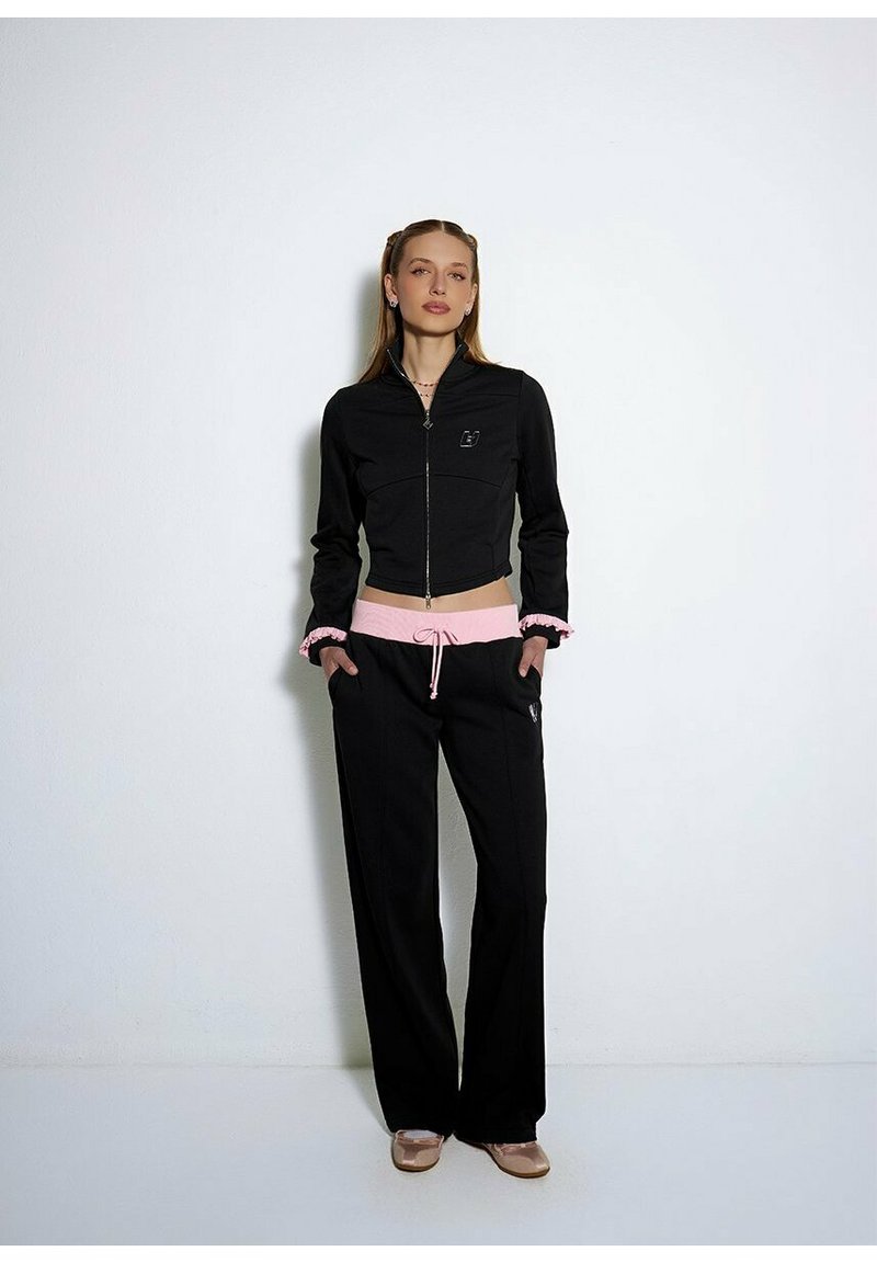 Czarna kurtka zapinana na zamek o dopasowanym kroju, z różowym sznurkiem w pasie, w połączeniu z czarnymi spodniami z bocznymi kieszeniami i teksturowanym wykończeniem.