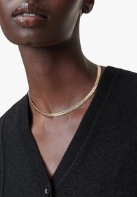 Gul choker halskæde med en glat, skinnende tekstur, båret med en sort, struktureret cardigan med V-udskæring og knaplukning.