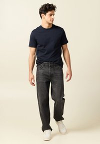 T-shirt in cotone navy abbinato a jeans grigi scuri. Sneaker bianche completano l'outfit. Design semplice, vestibilità rilassata e colori solidi.