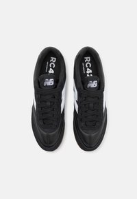 Pari musta-valkoisia New Balance RC 420 -tennareita, joissa on mustat nauhat, nähtynä ylhäältä valkoista taustaa vasten.