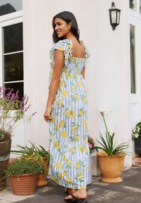 Maxiklänning i blå och vita ränder med gula citroner och blommönster. Har volangärmar och en figursydd bodice som flödar ner till ankellängd.