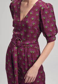 Vestido fucsia con patrón de hojas de palma verde, mangas cortas abullonadas, un escote en V profundo y un cinturón a juego con hebilla redonda en la cintura.