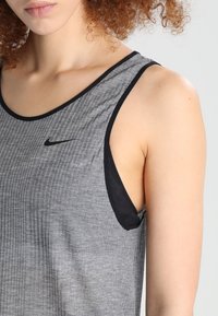 Grijze sporttanktop met een geribbeld patroon, voorzien van zwarte biezen en een klein zwart Nike-logo op het borstgebied.