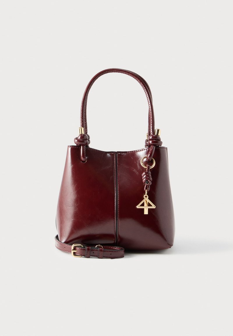 Geantă de mână din piele burgundy cu finisaj lucios, având două mâneruri, o curea detașabilă și un accesoriu auriu în formă de breloc.