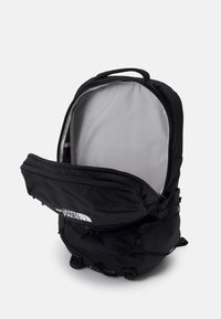 Schwarzer Rucksack mit einer großen Reißverschlussöffnung, grauer Innenauskleidung und verstellbaren Trägern. Verfügt über ein auffälliges Logo auf der Vorderseite sowie seitliche Schnallen.