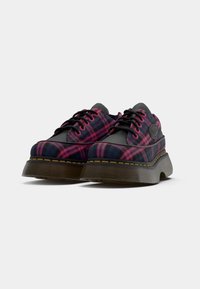 Plaid sneakers in navy, pink, and black fabric with black laces and a thick textured sole. Features a yellow stitching detail.