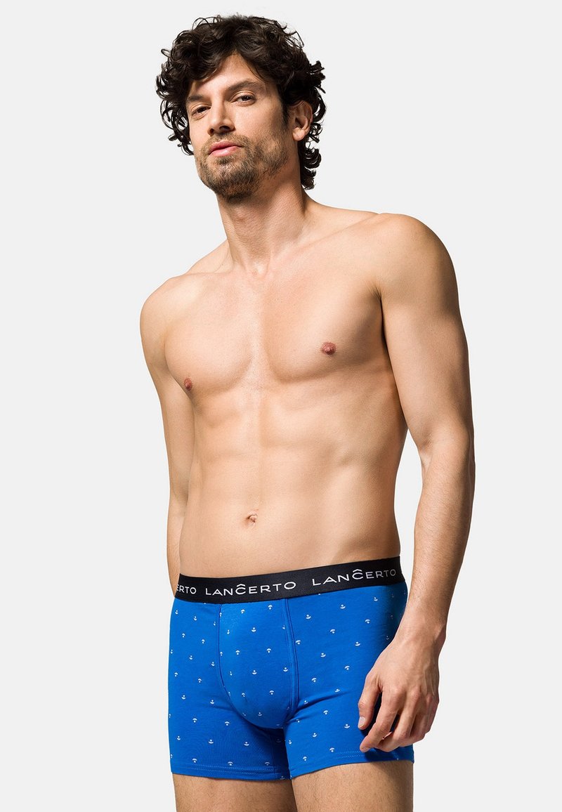 Niebieskie bawełniane bokserki z czarnym paskiem, na którym widnieje nazwa marki. Tkanina ma subtelny wzór z małymi białymi kształtami.