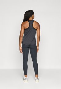 Débardeur de sport noir avec un design dos nageur, associé à un legging noir. Le modèle porte des baskets argentées, montrant une silhouette ajustée.