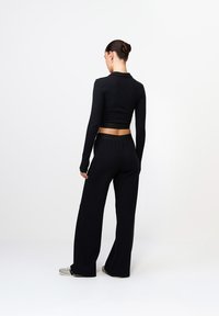 Fekete, hosszú ujjú crop top, széles lábú nadrággal párosítva, mindkettő puha anyagból készült. A derékpánton finom logó részlet található.