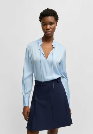 Camicia di seta blu chiaro con scollatura a V profonda e maniche lunghe, abbinata a una gonna blu scuro con vita alta e bottoni laterali.