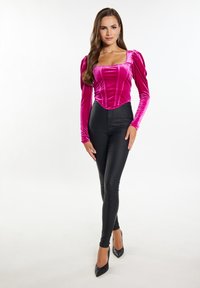 Body in velluto fucsia con scollo quadrato e maniche a sbuffo abbinato a leggings neri a vita alta e tacchi a punta neri.
