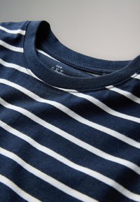 T-shirt en coton bleu marine avec des rayures blanches horizontales et un col rond, posé à plat sur une surface claire.